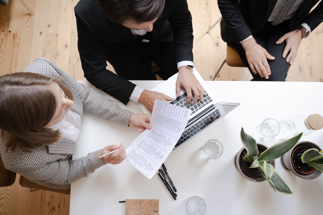 Overhead view of colleagues collaborating at a desk with laptop and documents in a business meeting.